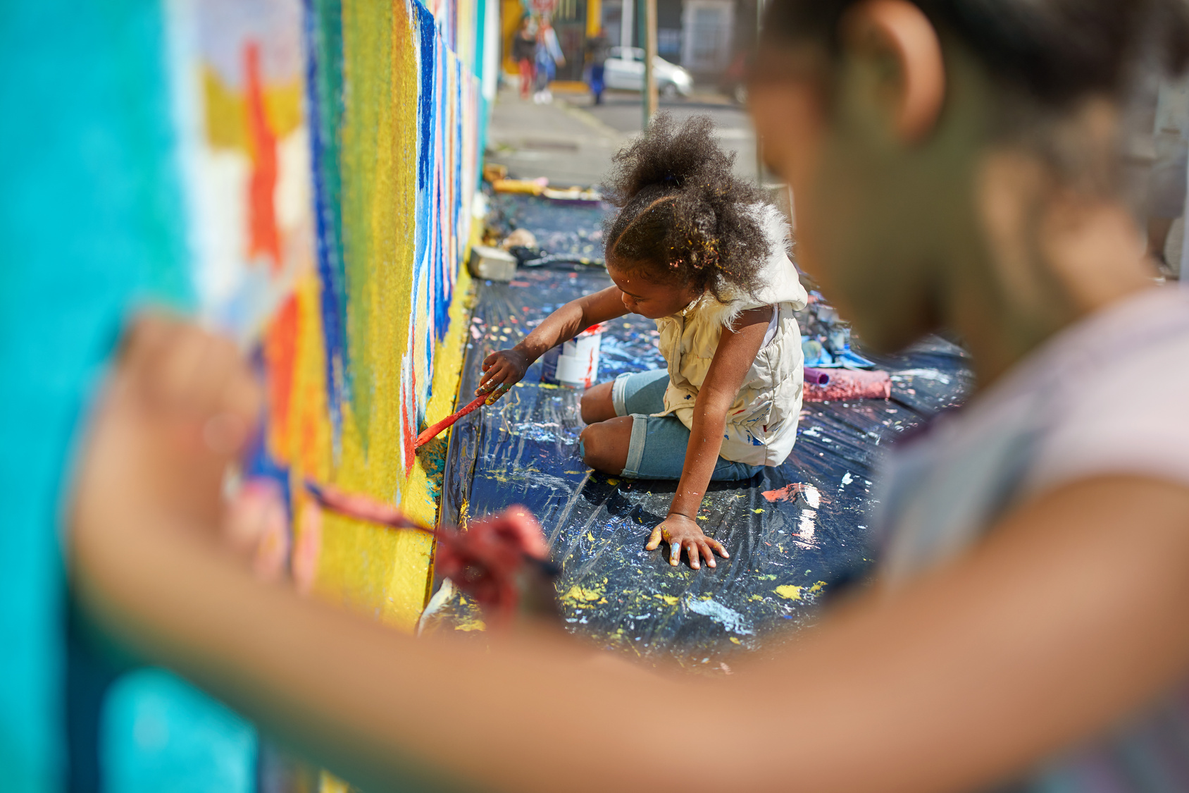 Niña pintando un mural comunitario urbano junto a voluntarios
